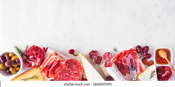 Variety of cheese and meat appetizers. Top view bottom border on a white marble banner background with copy space.