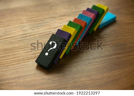 A variety color of fallen wooden domino with a symbol of question on wooden background.
