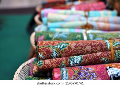 Variety of colorful batik fabrics scrolls in a basket at street bazaar 