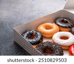 A variety of colorful donuts arranged in a box, featuring a mix of glazed, chocolate-coated, and sprinkled toppings. The assortment includes donuts with vibrant green, white, red, and chocolate