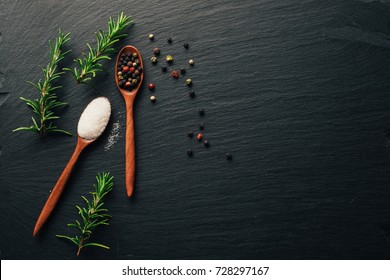 Variety of colorful spices in wooden spoons. Salt flakes, mixed pepper, and fresh rosemary on dark black slate background. Top view. Copy space. - Powered by Shutterstock