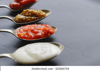 Variety of condiments on vintage spoons on slate background, mayonnaise, tomato sauce, mustard and sweet chilli jam