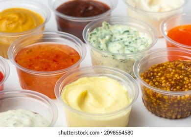 Variety of different sauces and condiments in small cups on white table. Mayonnaise, cheese sauce, pesto, mustard, sweet and sour sauces.