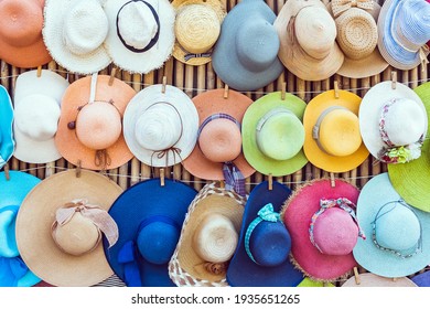 A variety of fashionable and colorful hats hanging on the bamboo backdrop of curbside shop.Women's designer hats from the sun of different colors. Design of women's beach hats. Beach hats for summer. - Powered by Shutterstock