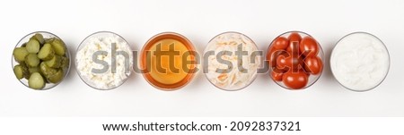 A variety of fermented foods for gut health. Bowls on a white background. Cucumbers, tomatoes, sauerkraut, yogurt, cottage cheese, apple cider vinegar. Banner.