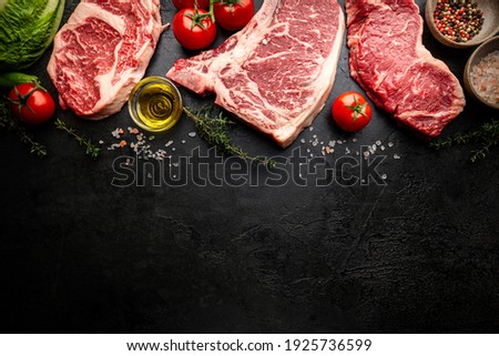 Variety of Fresh Raw Black Angus Prime Meat Steaks T-bone, New York, Ribeye and seasoning on black background, top view
