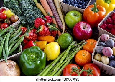 Variety of fresh raw organic fruits and vegetables in light brown containers sitting on bright blue wooden background