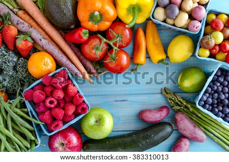 Variety of fresh raw organic fruits and vegetables in light blue containers sitting on bright blue wooden background