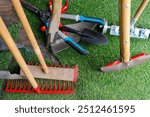 A variety of garden tools positioned on artificial grass for outdoor gardening. Several garden tools, including a rake, shovel, and pruners, are arranged on a patch of artificial grass.