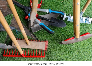 A variety of garden tools positioned on artificial grass for outdoor gardening. Several garden tools, including a rake, shovel, and pruners, are arranged on a patch of artificial grass. - Powered by Shutterstock