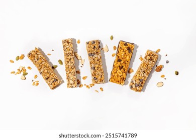 A variety of granola bars on a white surface with scattered nuts and seeds, healthy snacks, overhead view - Powered by Shutterstock