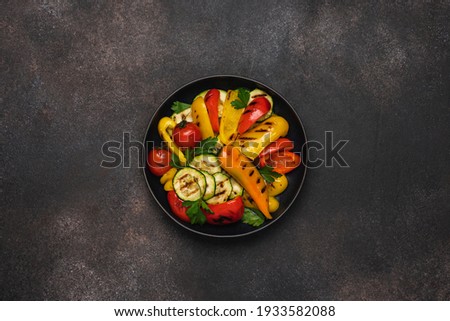 Variety of grilled vegetables in bowl on black background. Zucchini, bell peppers, hot peppers, tomatoes and green parsley