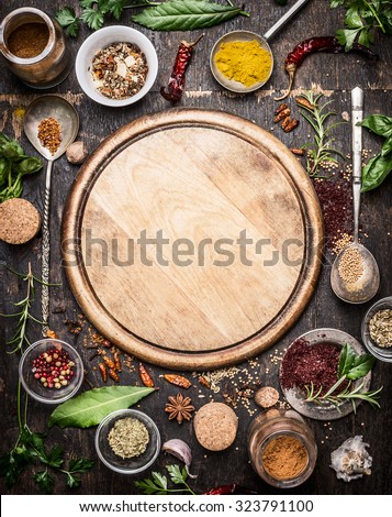 variety of herbs and spices  around empty cutting board on rustic wooden background, top view.Creative and national cuisine  and cooking concept.