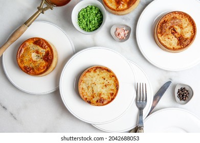 Variety Of Home Made Traditional Baked Pies With Pastry Crust, Green Peas And Salt And Pepper, Photographed From An Overhead View On White Ceramic Plates And White Marble Texture Kitchen Counter.