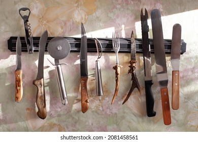 Variety Of Kitchen Knives, Spatulas And Other Kitchen Tools Hanging On Magnetic Strip Or Holder On The Wall 