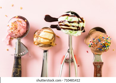 Variety of metal ice cream scoops with different ice cream and toppings on pink background.