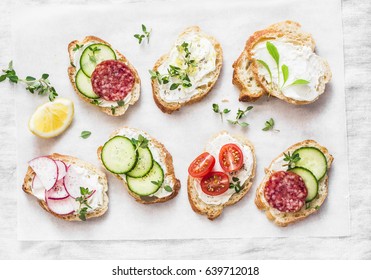 Variety of mini sandwiches with cream cheese, vegetables and salami. Sandwiches with cheese, cucumber, radish, tomatoes, salami, thyme, lemon zest on a light 
 background, top view. Flat lay    - Shutterstock ID 639712018