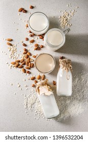 Variety Of Non-dairy Vegan Lactose Free Nuts And Grain Milk Almond, Hazelnut, Coconut, Rice, Oat In Glass Bottles With Ingredients Above Over White Spotted Background. Flat Lay, Space