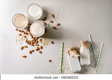 Variety Of Non-dairy Vegan Lactose Free Nuts And Grain Milk Almond, Hazelnut, Coconut, Rice, Oat In Glass Bottles With Straws And Ingredients Above Over White Spotted Background. Flat Lay, Space