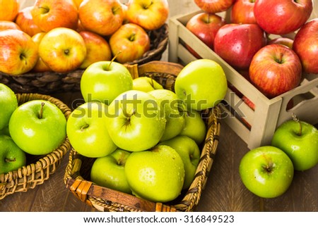 Variety of organic apples in baskets on wood table.