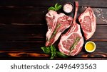 Variety of raw beef meat steaks for grilling with seasoning: Tomahawk steak, Ribeye, Ossobuco and T-bone steak, on a wooden brown background.