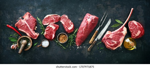 Variety of raw beef meat steaks for grilling with seasoning and utensils on dark rustic board - Shutterstock ID 1707971875