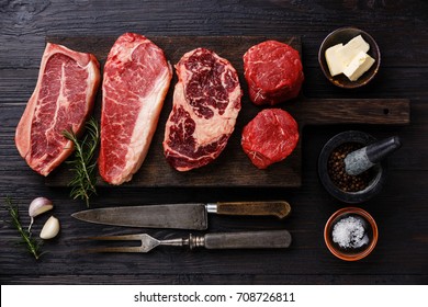 Variety Of Raw Black Angus Prime Meat Steaks Blade On Bone, Striploin, Rib Eye, Tenderloin Fillet Mignon On Wooden Board And Seasoning