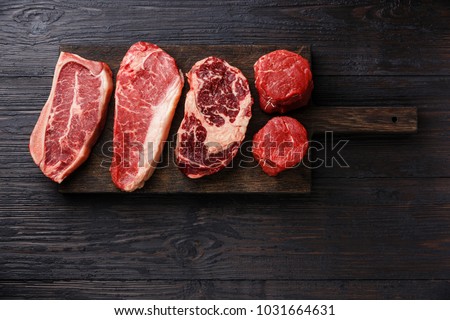 Variety of Raw Black Angus Prime meat steaks Blade on bone, Striploin, Rib eye, Tenderloin fillet mignon on wooden board copy space