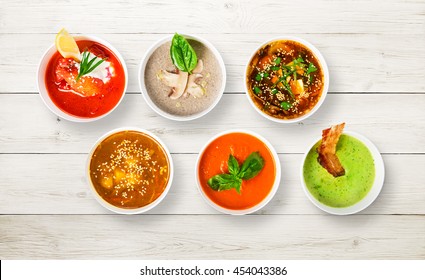 Variety Of Restaurant Hot Dishes, Healthy Food. Japanese Miso Soup, Asian Fish Soup, Russian Borscht, English Pea Soup With Bacon, Mushroom Soup, Spanish Gazpacho At White Rustic Wood, Top View