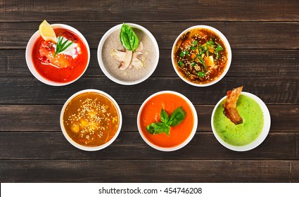 Variety Of Restaurant Hot Dishes, Healthy Food. Japanese Miso Soup, Asian Fish Soup, Russian Borscht, English Pea Soup With Bacon, Mushroom Soup, Spanish Gazpacho At Brown Rustic Wood, Top View