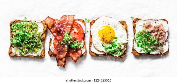 Variety of sandwiches for breakfast, snack, appetizers - avocado puree, fried egg, tomatoes, bacon, cream cheese, smoked mackerel grilled whole grain bread sandwiches. On a light background, banner   - Powered by Shutterstock