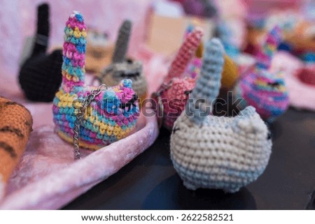 A variety of small, crocheted cat keychains in different colors are displayed on a soft pink surface at a market