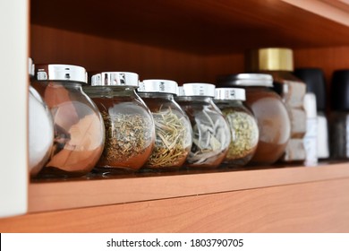 Variety spice jars on a shelf. Kitchen shelf with glass jars filled different organic herbs and spices, selective focus. Domestic kitchen. Health Food herbs, seeds in spice jars.