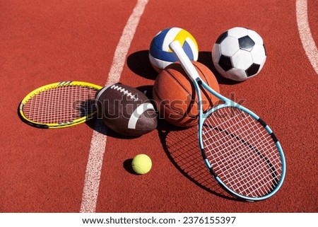 A variety of sports equipment including an american football, a soccer ball, a tennis racket, a tennis ball, and a basketball