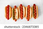 Variety of unique hot dogs with an assortment of toppings. Overhead view on a white marble background.