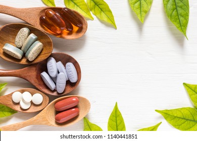 Variety of vitamin pills in wooden spoon on white background with green leaf, supplemental and healthcare product, flat lay surface