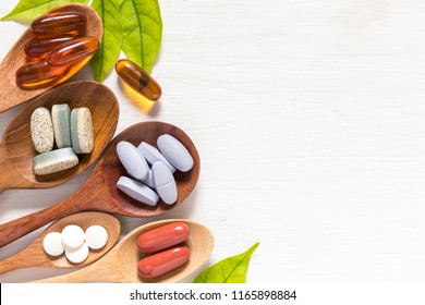 Variety of vitamin pills in wooden spoon on white background with green leaf, supplemental and healthcare product, flat lay surface - Shutterstock ID 1165898884