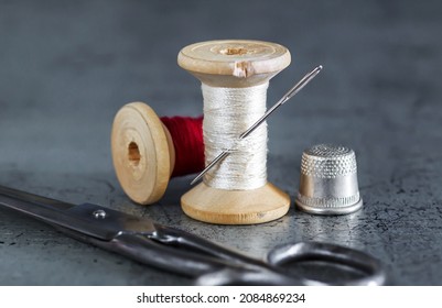 Various accessories for needlework. A set of sewing tools, spools of thread, fabrics, scissors and a thimble on an old surface. Retro style