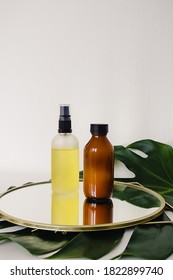 Various amber and matte glass bottles for cosmetics, natural medicine , essential oils or other liquid on a white background standing on a mirror decorated with a green monstera leaf - Shutterstock ID 1822899740