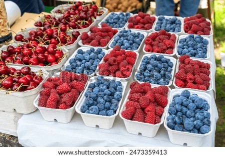 Various baskets filled with fresh cherries, raspberries, and blueberries at a market stall, showcasing vibrant colors and textures