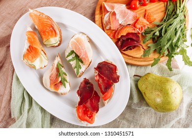 Various Bread Ham Canape Snack Top Down Flat Lay. Pork Dried Prosciutto And Salmon Sliced Meat On Italian Small Sandwich Appetizer. Tasty Jamon On White Plate. Delicatessen Toast Bruschetta Flatlay