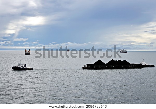 Various bulk carriers, vessels, and tugboats\
in port under cargo operations and underway. Port of Muara Pantai,\
Indonesia, January,2021