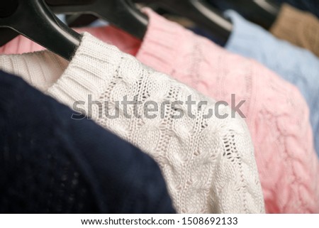 Various cable knit sweaters or pullovers on hanger rack in a clothes store or at a wardrobe, selective focus