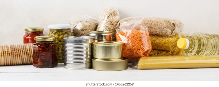 Various Canned Food And Raw Cereal Grains On A Table. Set Of Grocery Goods For Cooking, Delivery Or Donation.