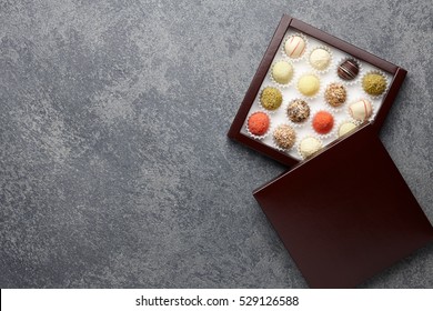 Various Chocolate Truffle Candies In A Box On Gray Stone Background