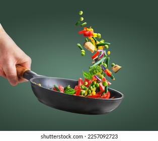 Diversas verduras picadas volando hacia una sartén en la mano del chef sobre fondo verde