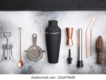 Various Cocktail Utensils.Copper Jigger,straw And Spoon With Black Shaker,muddler And Strainer On Light Board With Black Rubber Tray.