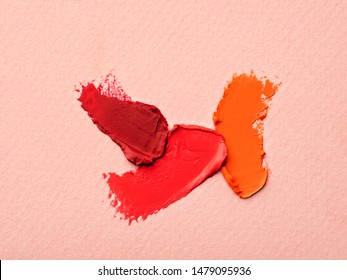 Various Color Lipstick Smears On Pale Pink Textured Background. Orange, Pink And Red Makeup Palette. Colorful Smudged Cosmetics Product. Makeup Creative Background.