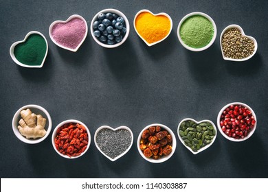Various colorful superfoods as acai powder, turmeric, matcha green tea, spirulina, quinoa, pumpkin seeds, blueberry, dried goji berries, cape gooseberries, raw cocoa, hemp seeds  on dark background