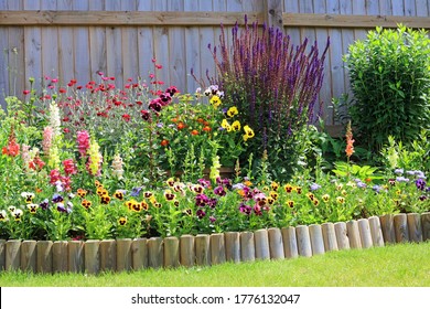 Various Colourful Flowers In A Garden Border With Wooden Fencing And Log Roll Lawn Edging.